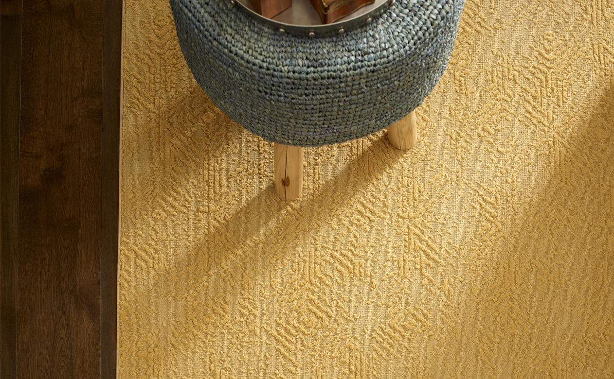 patterned yellow area rug in room with dark wood floors and gray stool